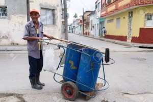 Cuban real man street sweeper. Worker pushing a garbage cart on narrow street.